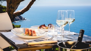 A dining table with plates of food, glasses of white wine, and a bottle of wine, overlooking a scenic ocean view.
