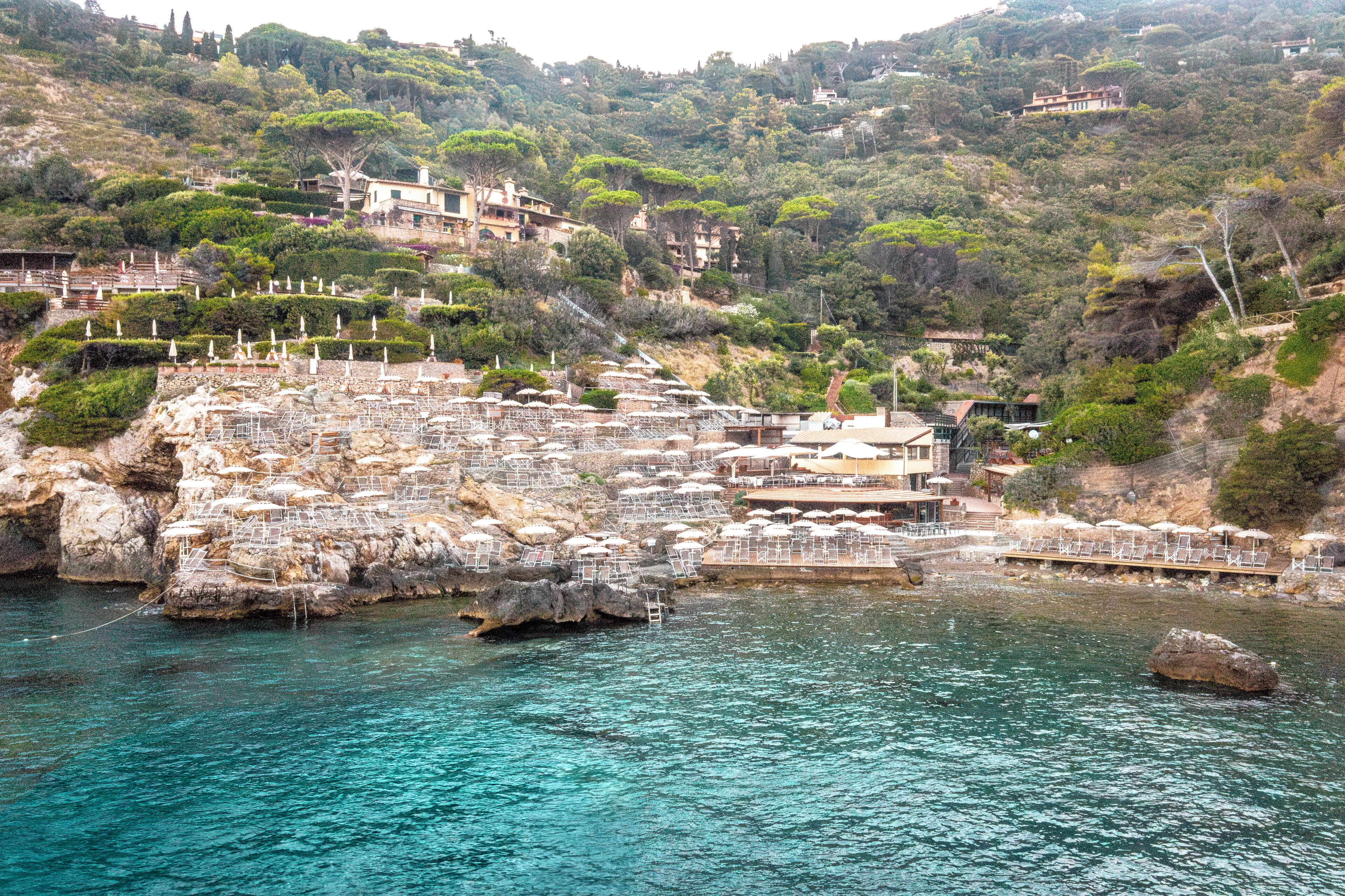A coastal hotel with multiple buildings, a rocky shoreline, and a pier with umbrellas.