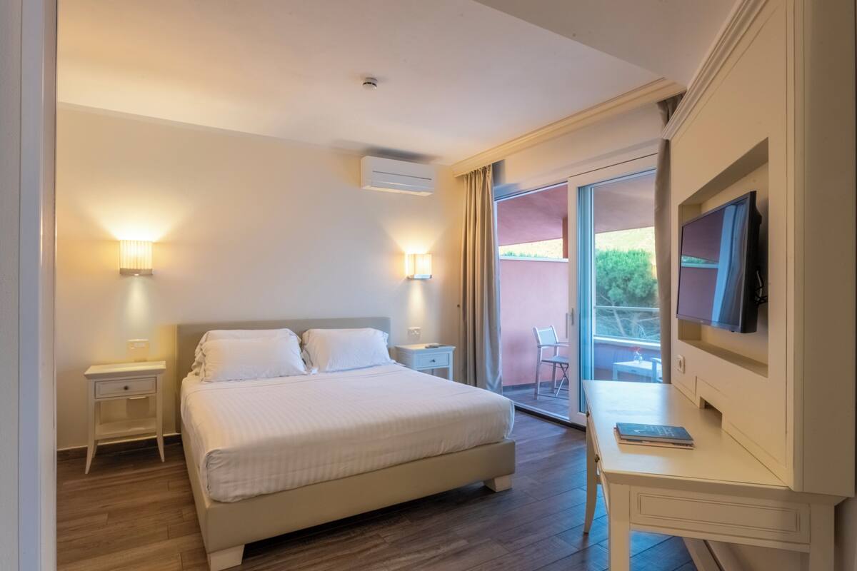 A hotel room with a large bed, bedside lamps, a desk with a chair, and a TV.