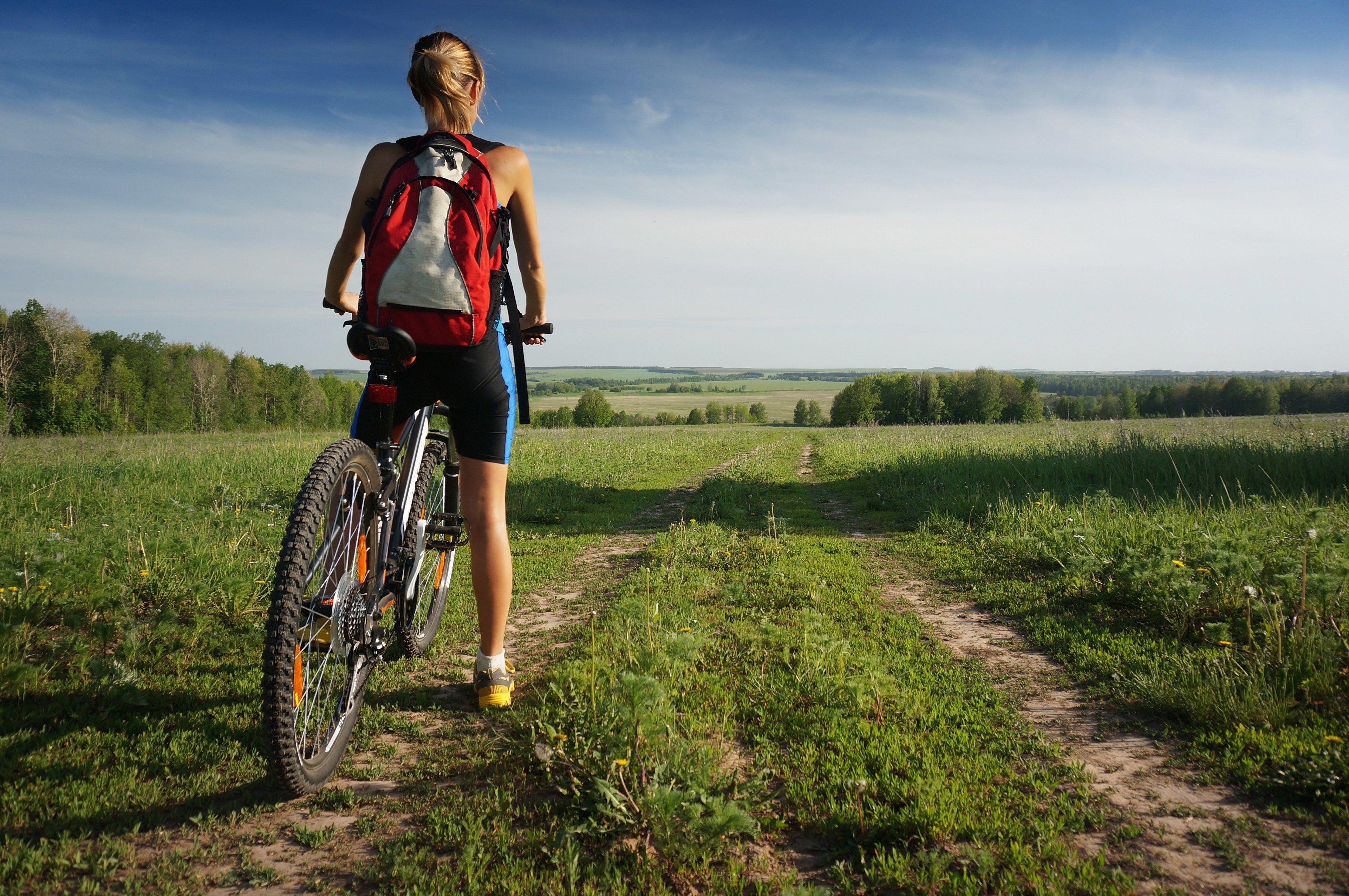 A person with a bicycle and a backpack on a dirt path in a grassy field.