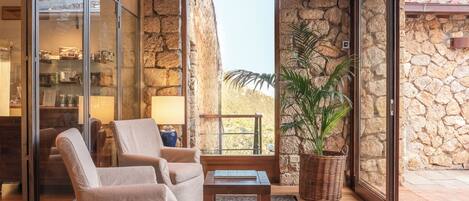 A modern interior with a stone wall, a glass display case, two beige armchairs, a small wooden table, and a potted plant.