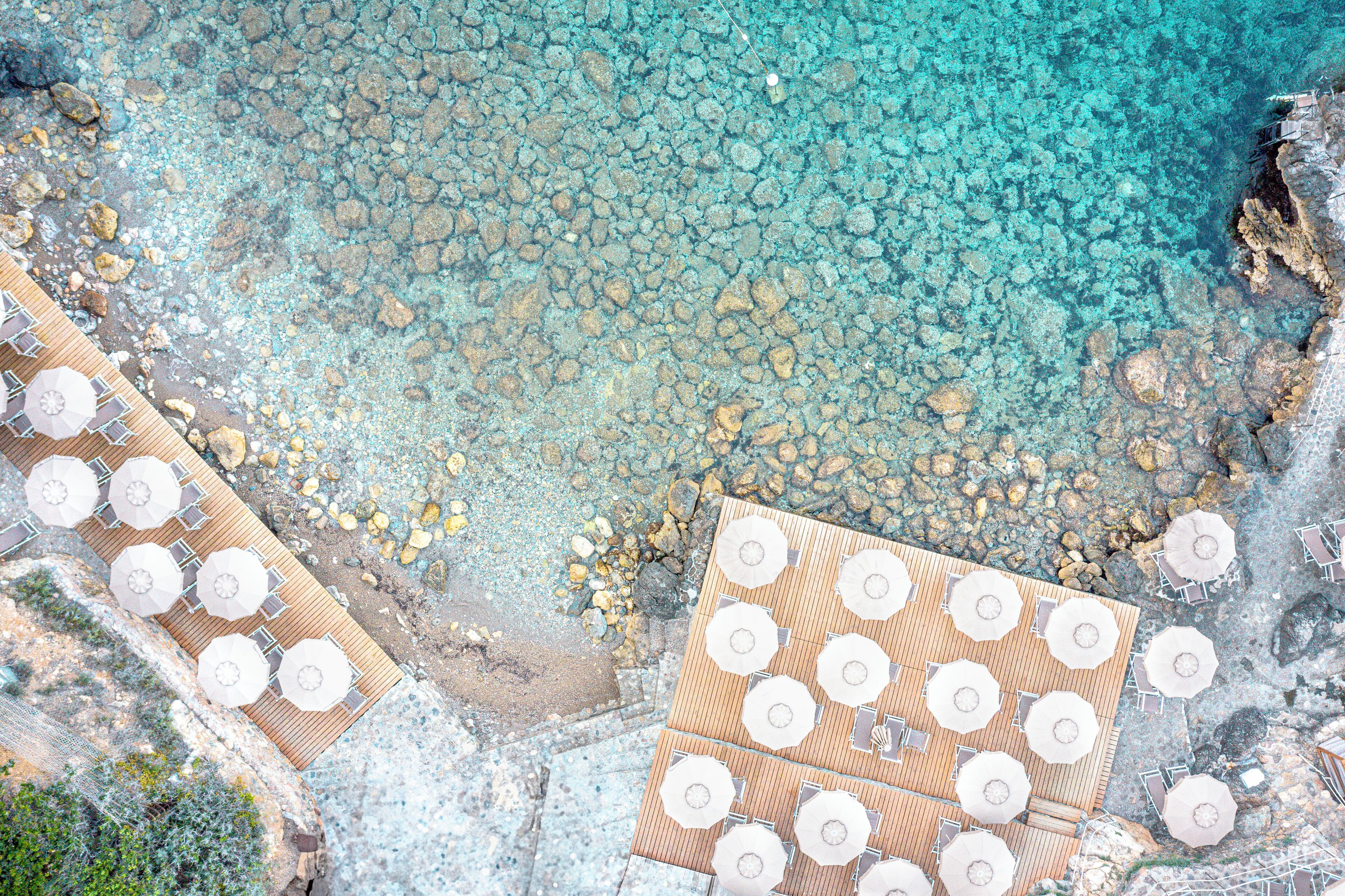 An aerial view of a beachside resort with multiple wooden deck areas, each equipped with umbrellas and seating.