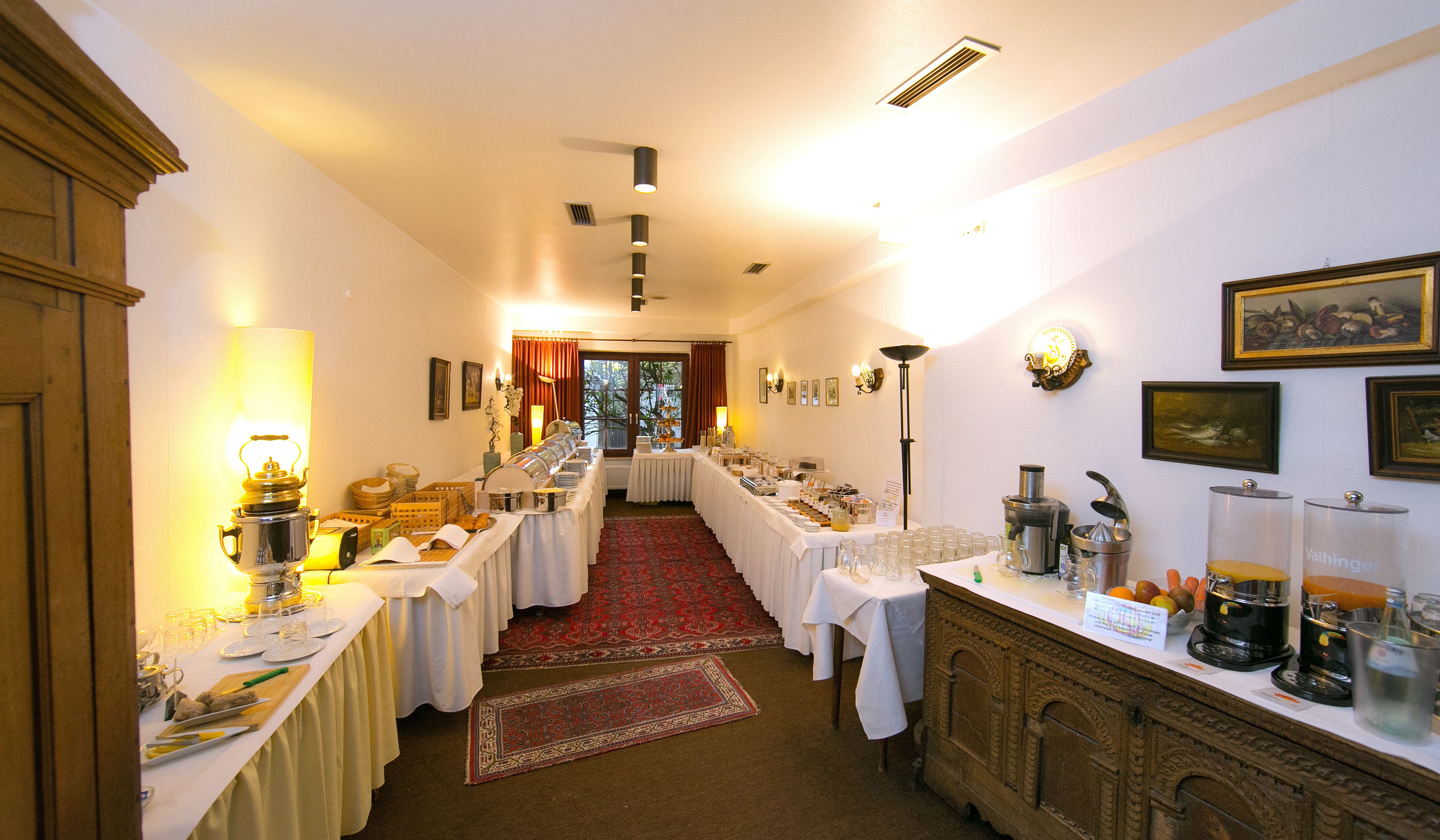 Un comedor de hotel con varias mesas dispuestas para el desayuno, una barra de buffet y un mostrador con diferentes dispensadores de comida y bebidas.