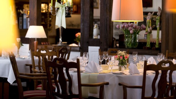 A dining area with wooden chairs, white tablecloths, and a chandelier. - Hotel Jägerhof (Langenhagen)