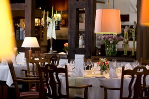 A dining area with wooden chairs, white tablecloths, and a chandelier. - Hotel Jägerhof (Langenhagen)