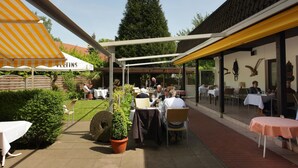 An outdoor patio area with tables and chairs, a yellow awning, and a sign that reads "Veltins." - Hotel Jägerhof (Langenhagen)