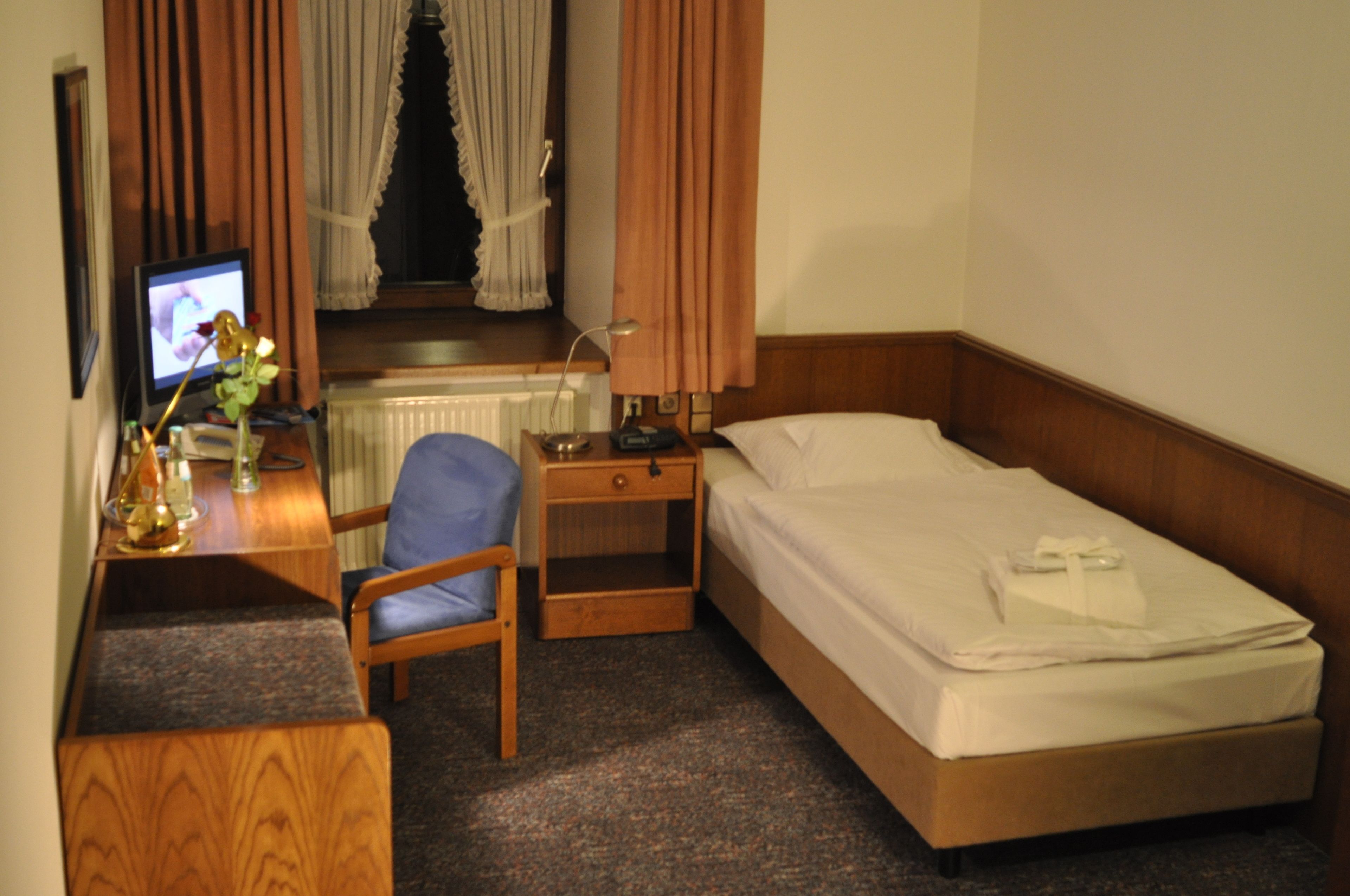 Quarto de hotel com uma cama, uma mesa de escritório com um computador, uma cadeira e uma janela com cortinas.