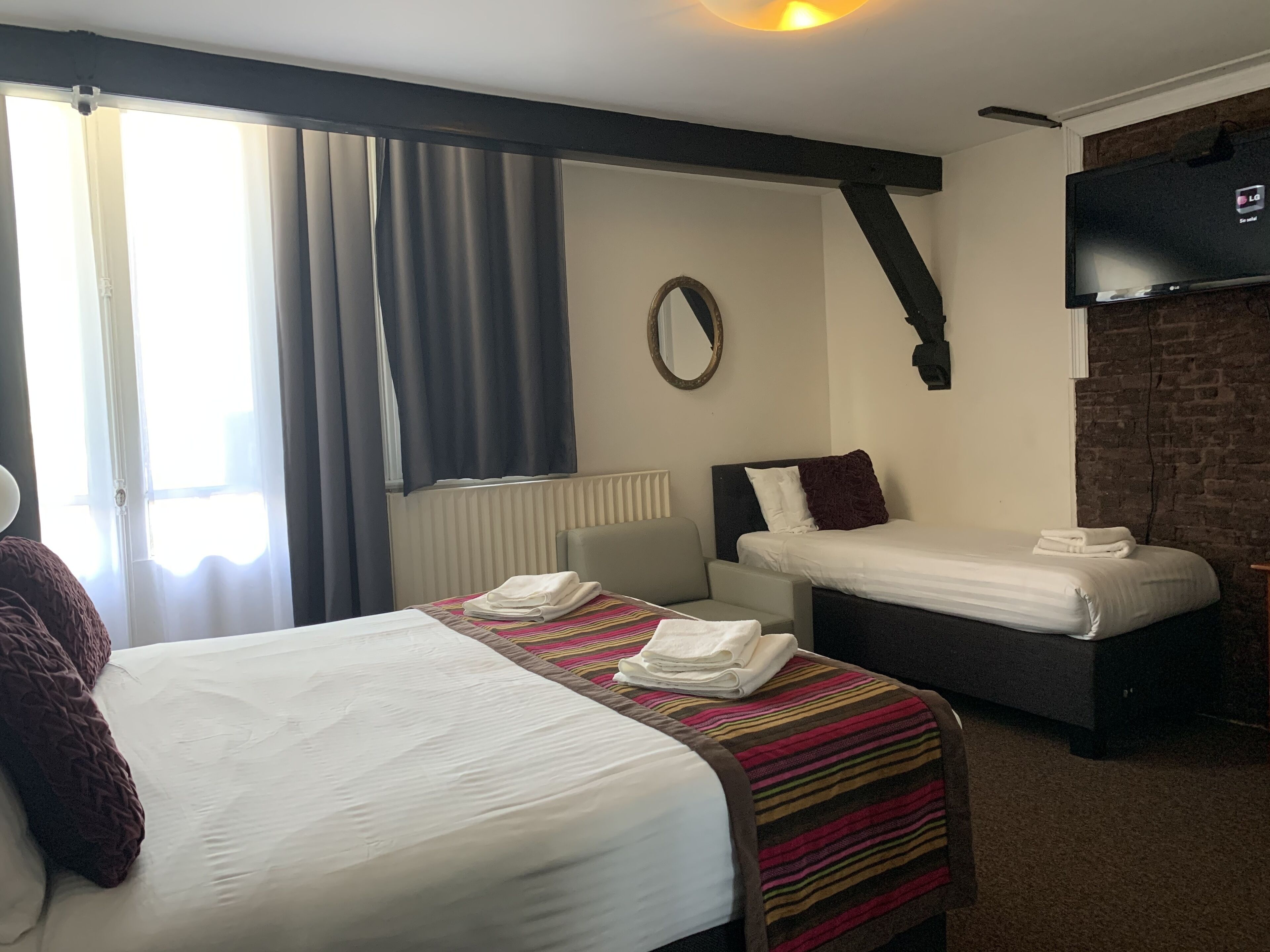 A hotel room with two beds, a TV, a mirror, and a window with curtains.