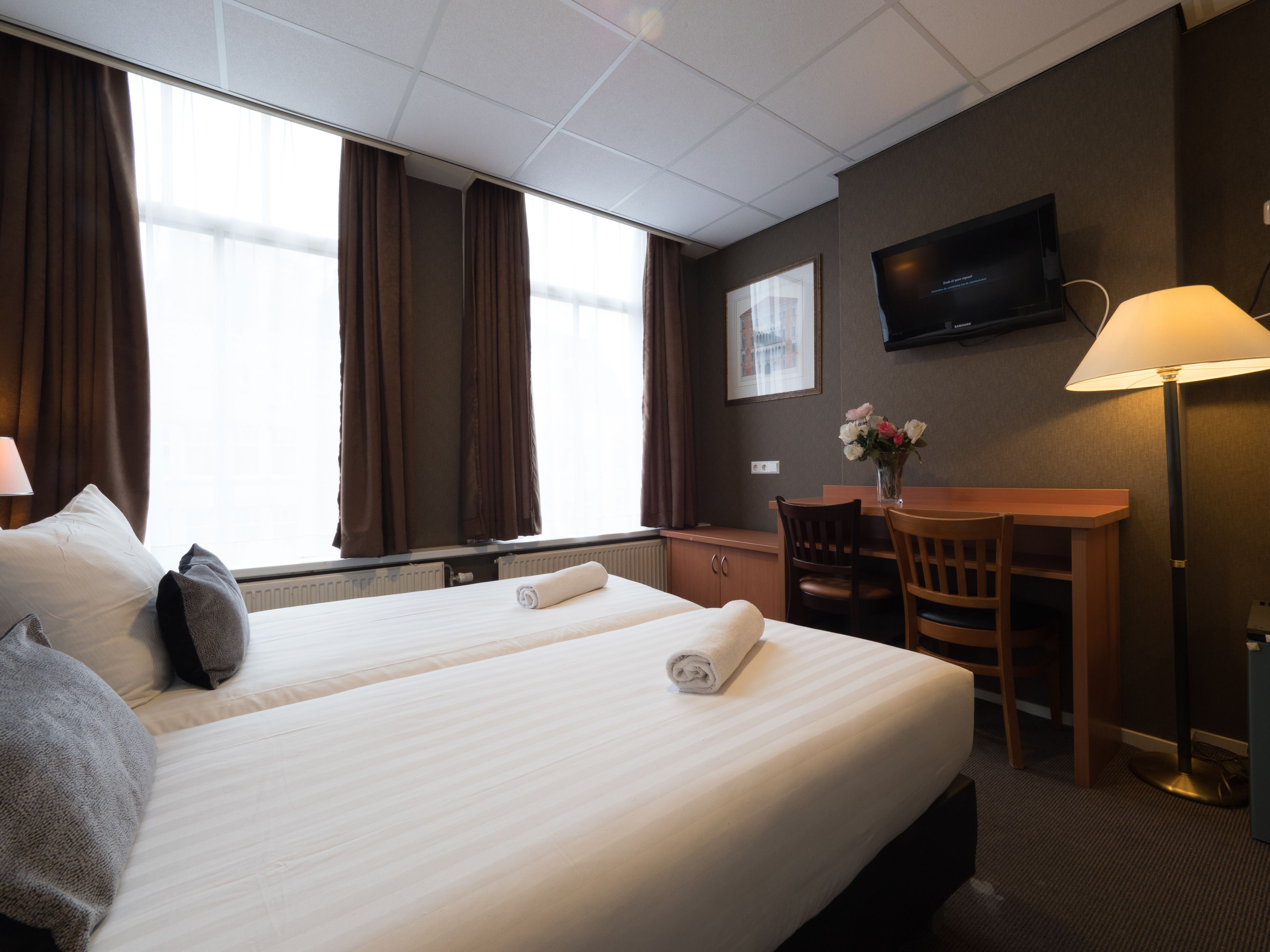 Una habitación de hotel con dos camas, un escritorio, una silla, un televisor y una lámpara.