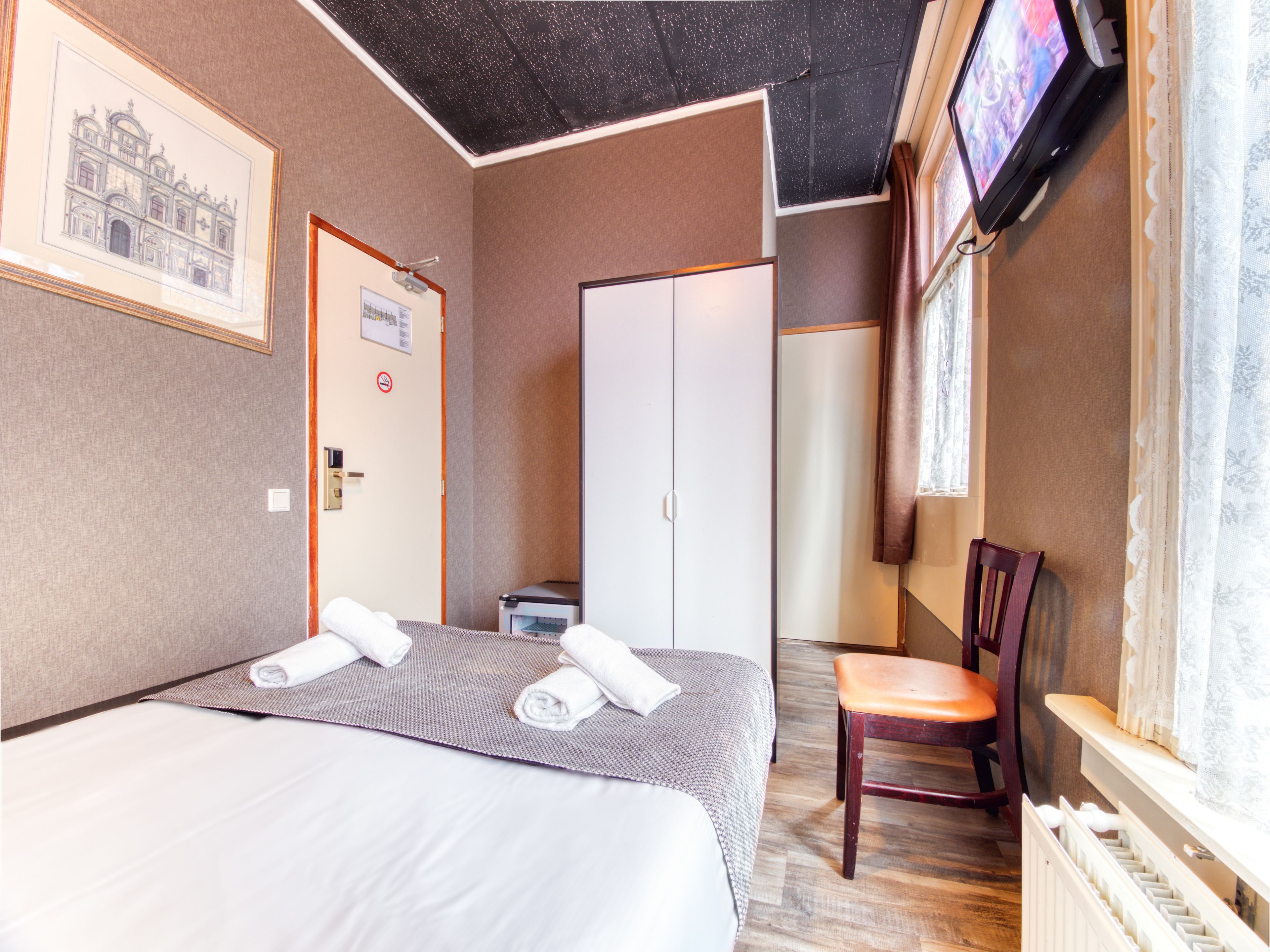 A hotel room with two beds, a desk, a chair, a television, and a framed picture on the wall.