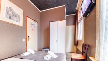 Habitación de hotel con dos camas, un escritorio, una silla, un televisor y un cuadro en la pared.