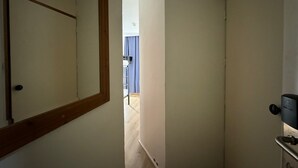 Een smalle gang met een houten deurkozijn links, een deur rechts, en een kijkje in een kamer met een blauw gordijn op de achtergrond.