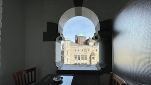 Een kamer met een tafel en stoelen, een raam met uitzicht op gebouwen, en een structuurwand.