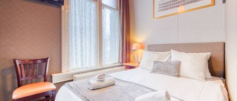 A hotel room with a bed, a chair, a TV, and a window with curtains.