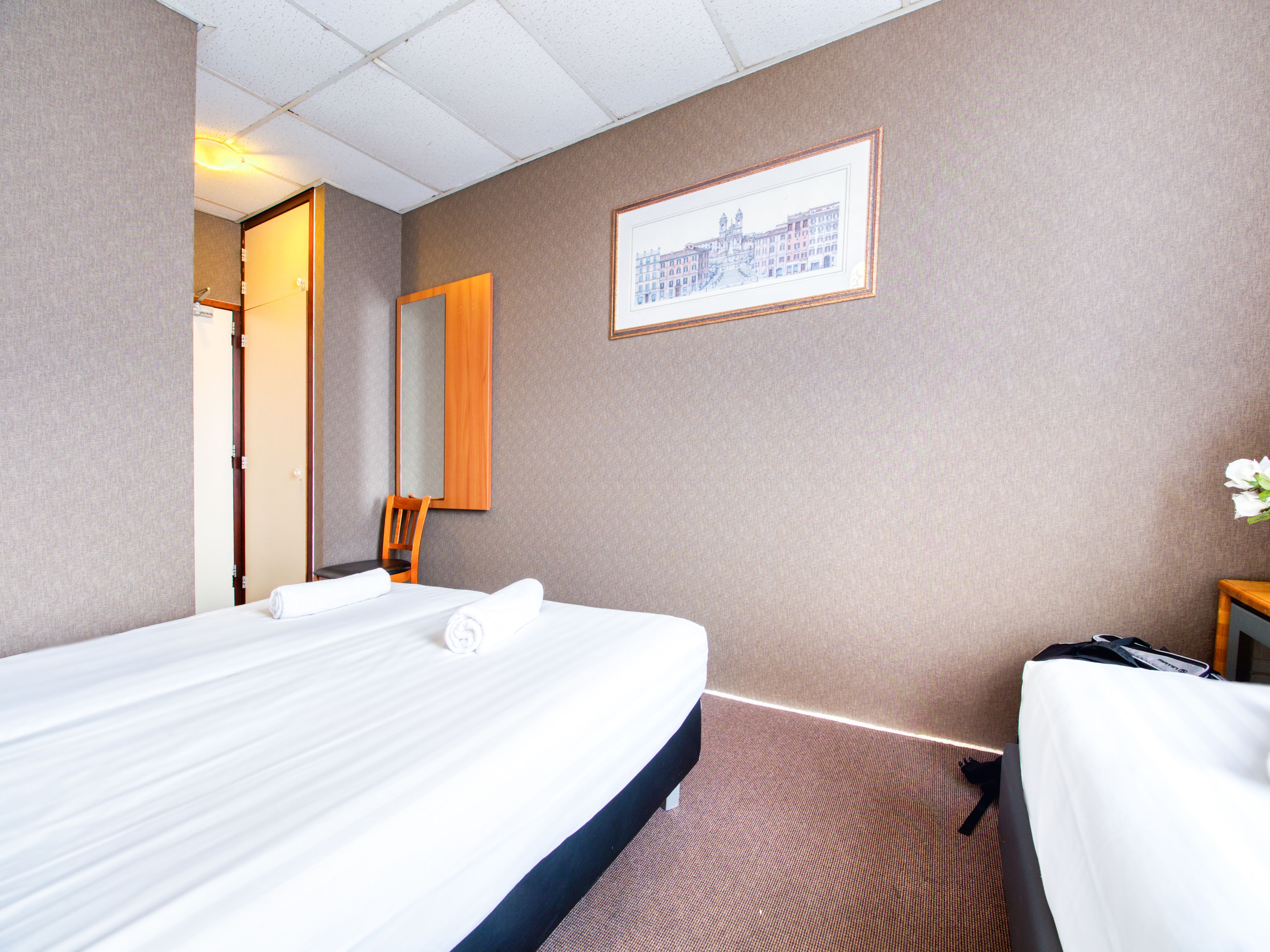 Een hotelkamer met een bed, een stoel, een bureau, een spiegel en een lijst met een foto aan de muur.