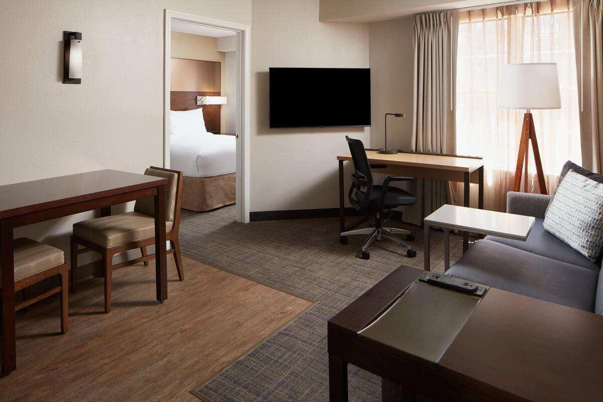A hotel room with a bed, a desk, a chair, a sofa, a TV, and a lamp.