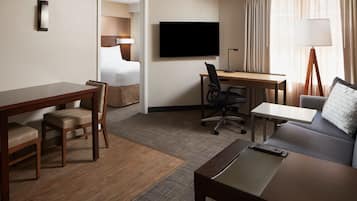 A hotel room with a bed, a desk, a chair, a sofa, a TV, and a lamp.