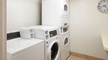 A laundry area with stacked washers and dryers, a control panel, and a clock on the wall.