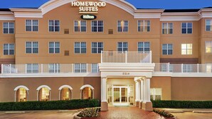 A large, multi-story hotel with a classic design, featuring a prominent entrance with a balcony and a sign that reads "Homewood Suites Hilton."