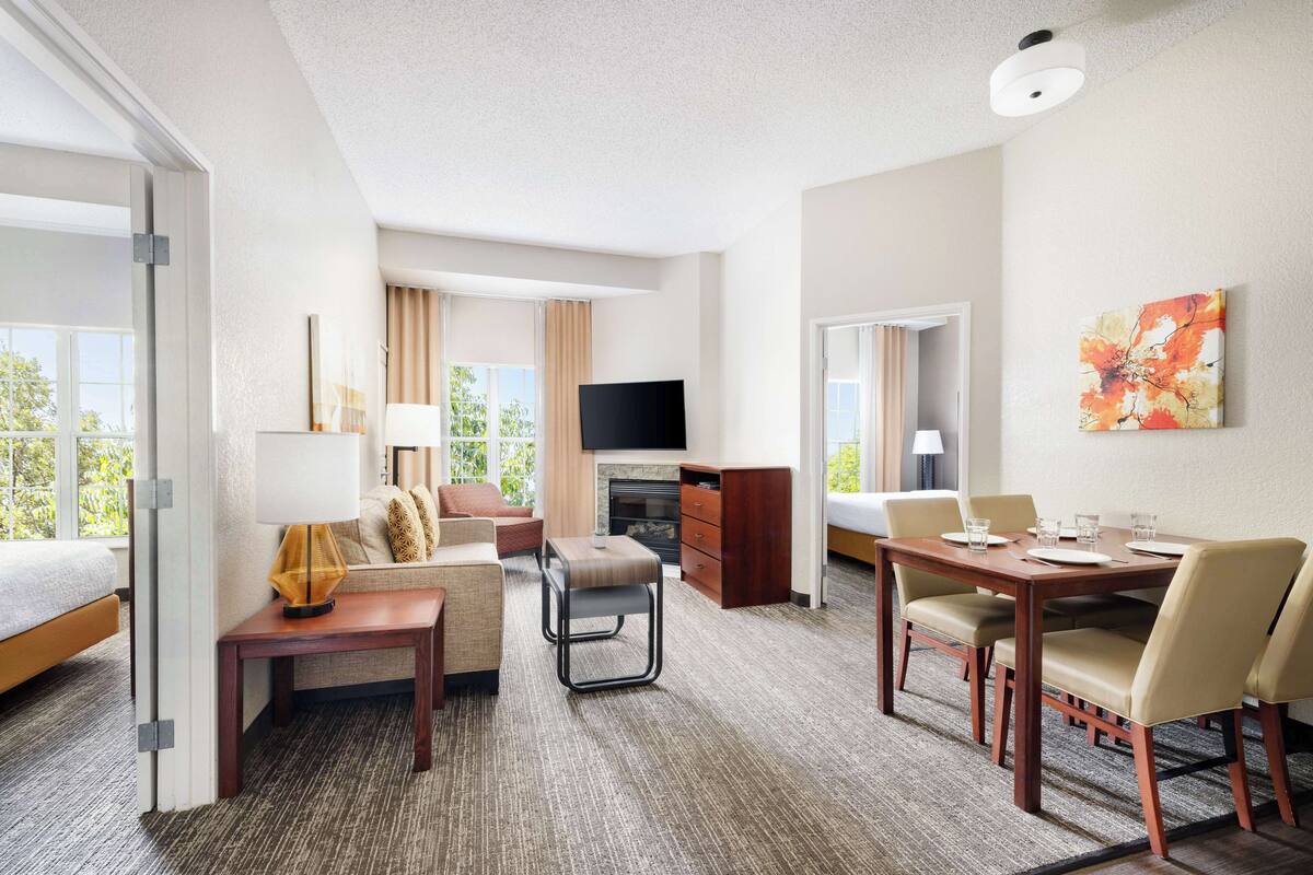 A hotel room with a bed, a sofa, a dining table with chairs, a TV, and a fireplace.