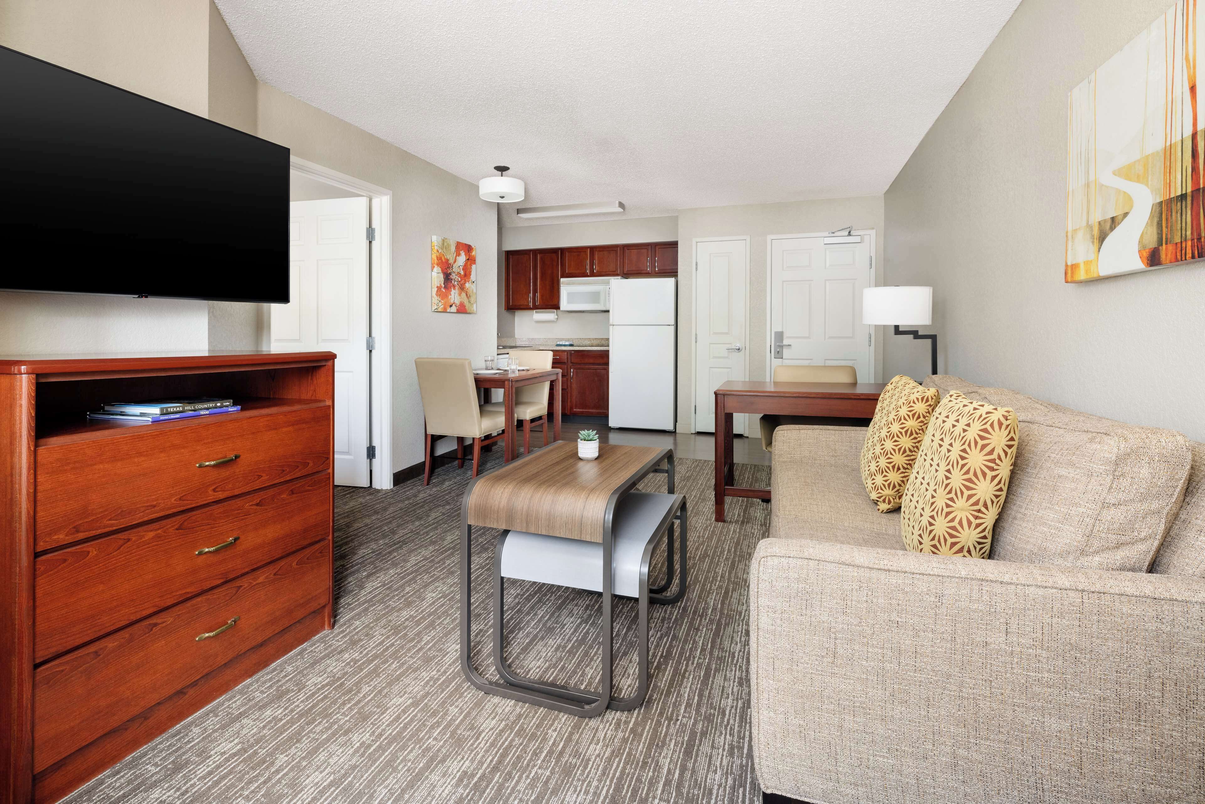A hotel room with a flat-screen TV, wooden dresser, sofa, and a kitchenette area.