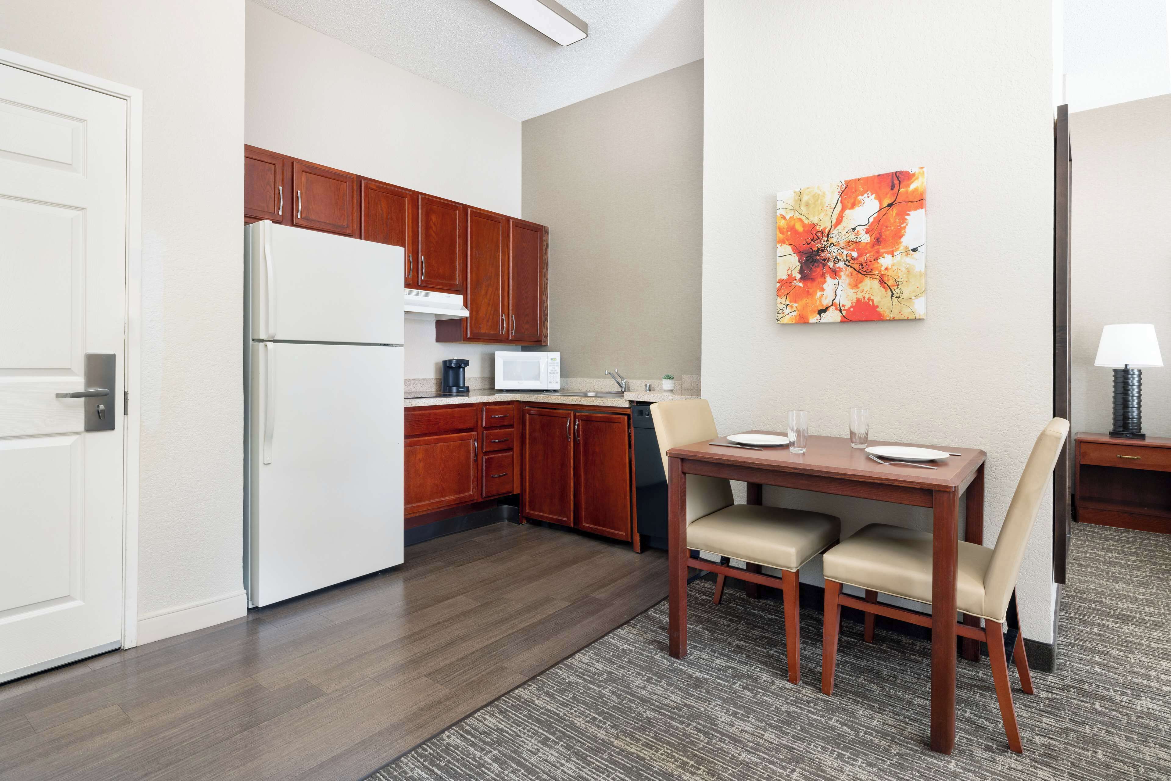 Una cocina compacta con armarios de madera, un refrigerador blanco, un microondas y una zona de comedor con mesa y sillas.