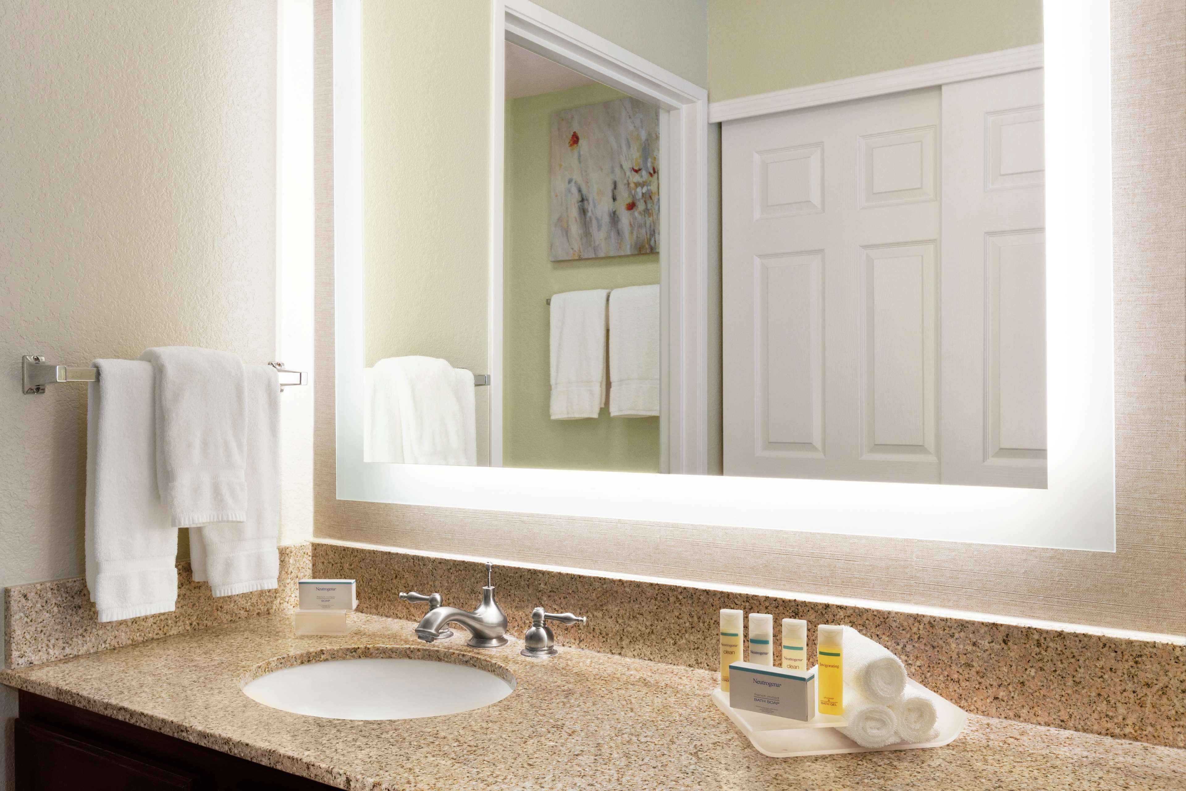 A bathroom with a granite countertop, a sink, a mirror, and a door.