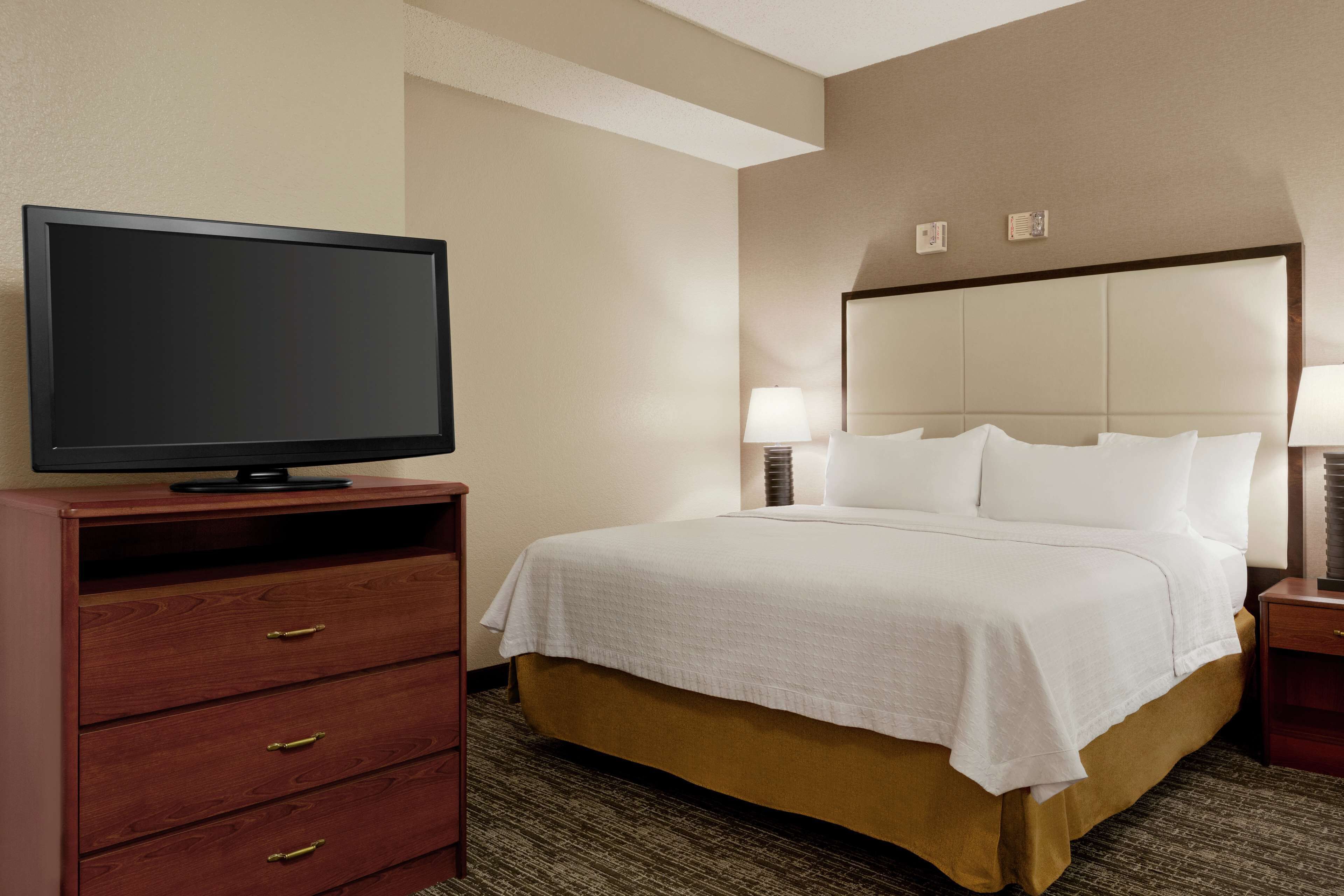 A hotel room with a bed, a television on a wooden dresser, and two bedside lamps.
