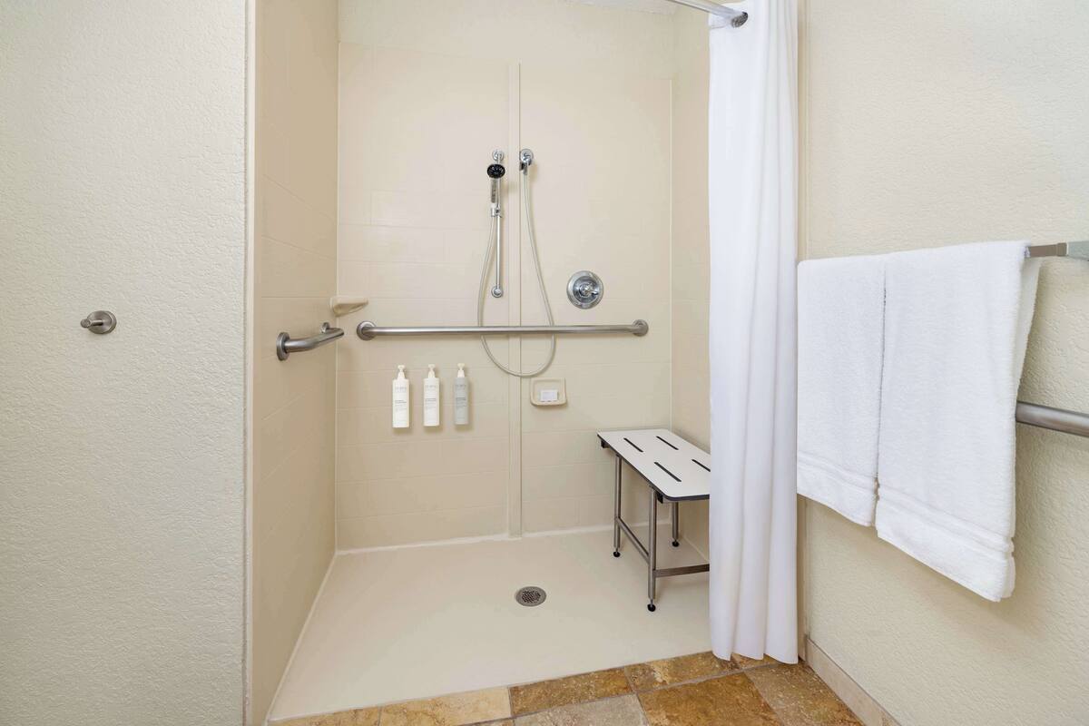 A handicap-accessible shower with a grab bar, a small bench, and hand sanitizer bottles.
