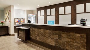 A hotel reception area with a counter, a minibar, a coffee machine, and a sign indicating Hilton Honors.