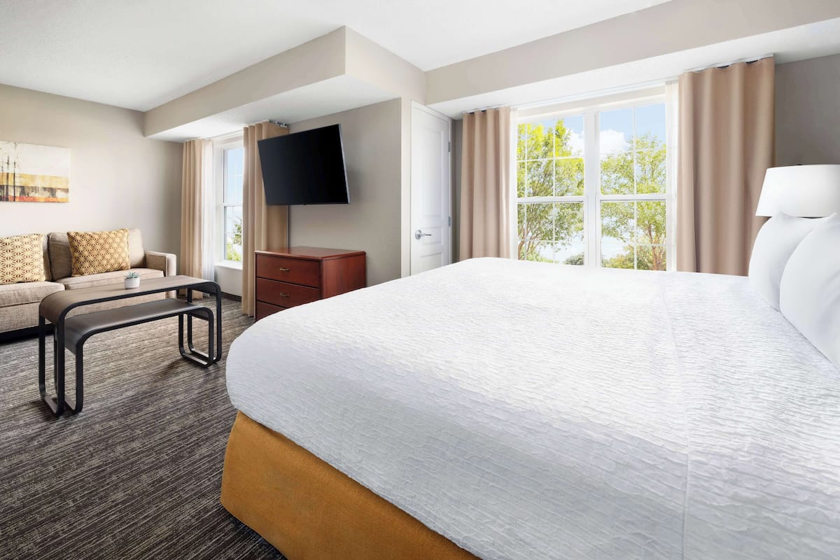 A hotel room with a large bed, a sofa, a TV, and a window with curtains.