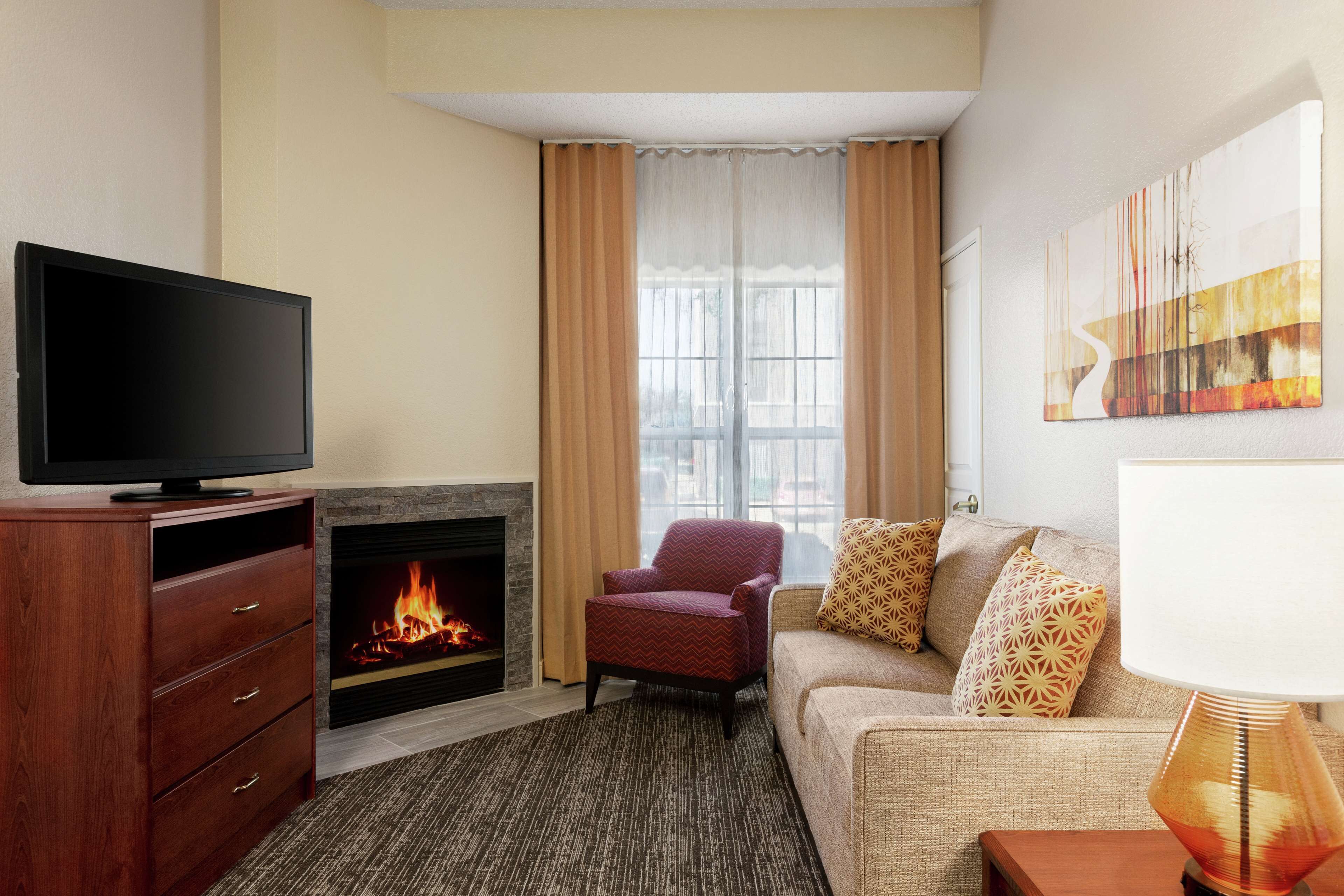 A living room with a flat-screen TV, a fireplace, a red armchair, a beige sofa with patterned cushions, and a modern lamp.