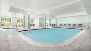 An indoor swimming pool with tiled flooring, a clear blue pool, and a seating area with tables and chairs.