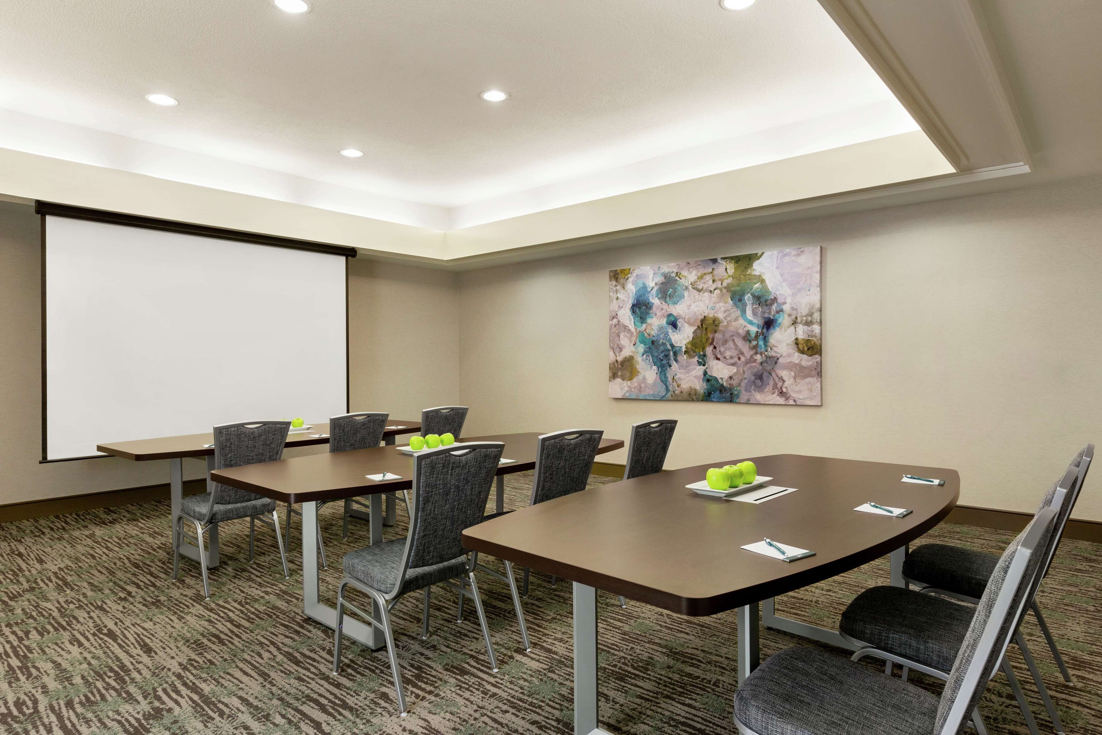 A conference room with a projector screen, a large abstract painting, and a carpeted floor.