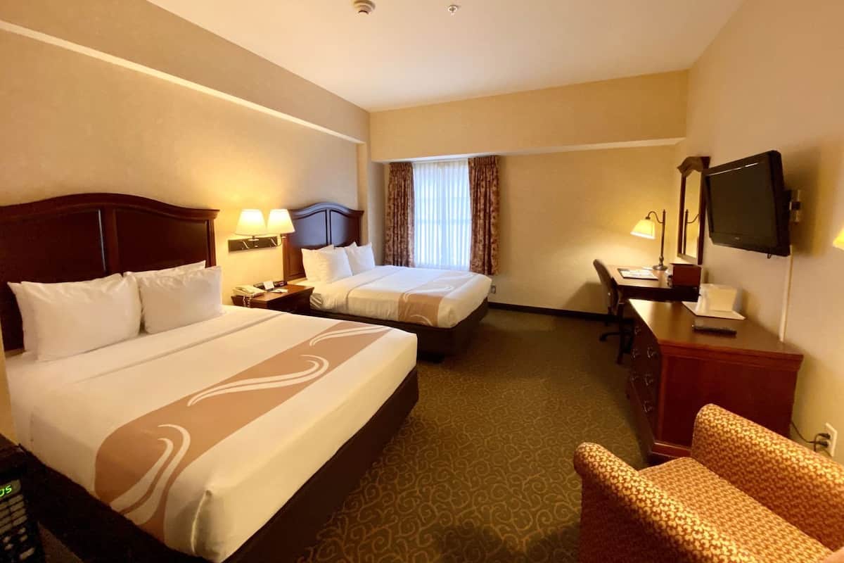 A hotel room with two beds, a desk, a chair, a television, and a window with curtains.