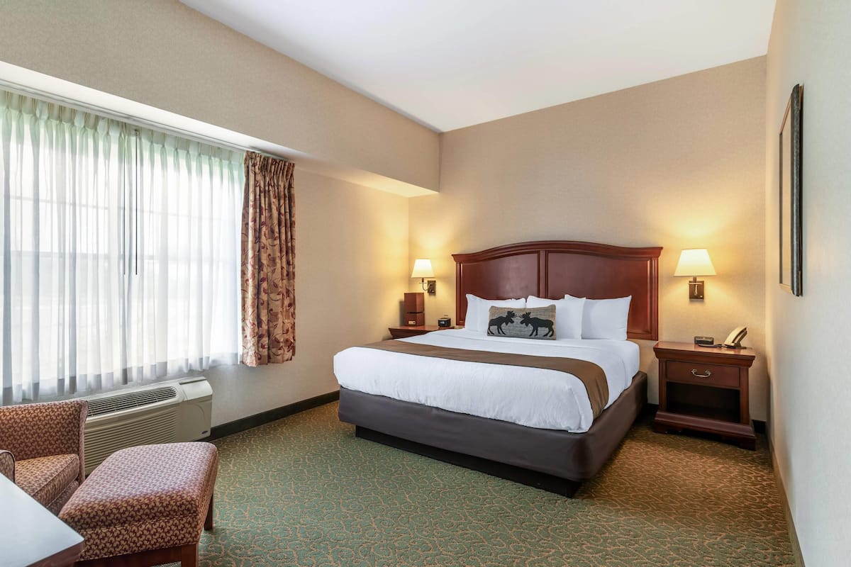 A hotel room with a large bed, two bedside tables with lamps, a chair, and a window with curtains.