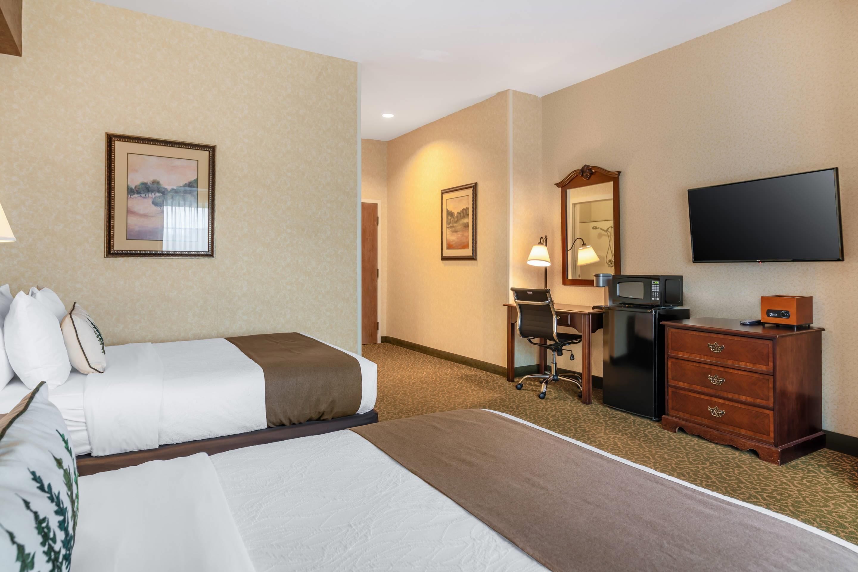 A hotel room with two beds, a desk, a television, and a dresser.