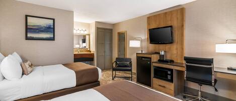 A hotel room with two beds, a desk, a chair, a TV, and a mirror.