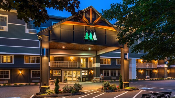 A hotel entrance with a prominent logo, a covered walkway, and a parking lot with marked spaces. - Maine Evergreen Hotel, an Ascend Collection Hotel (Augusta)