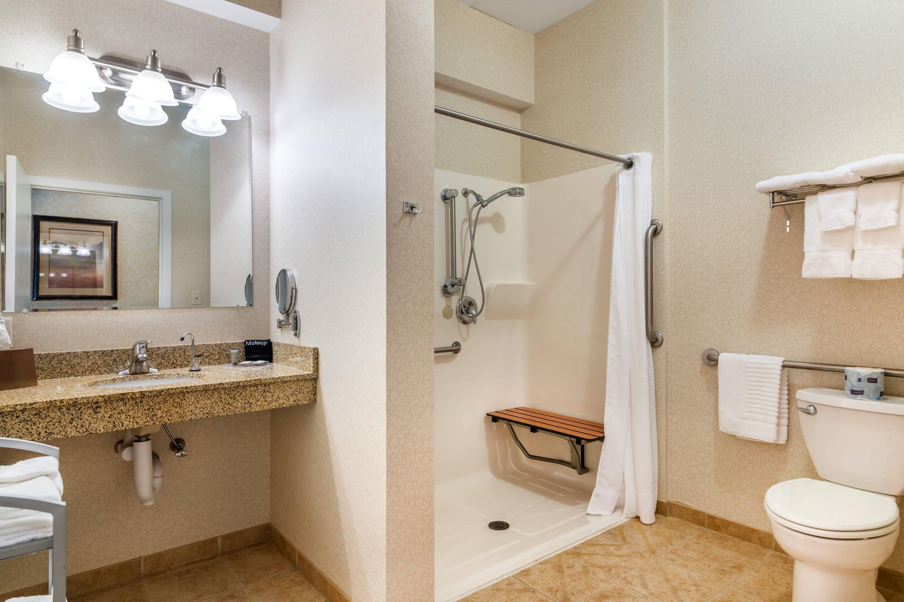 A bathroom with a sink, mirror, shower, toilet, and towel rack.