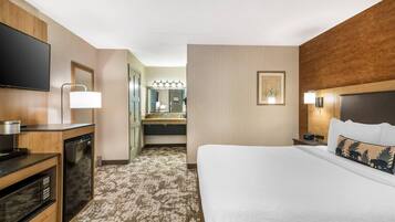 Habitación de hotel con cama, televisión, escritorio con microondas, lavabo y espejo.
