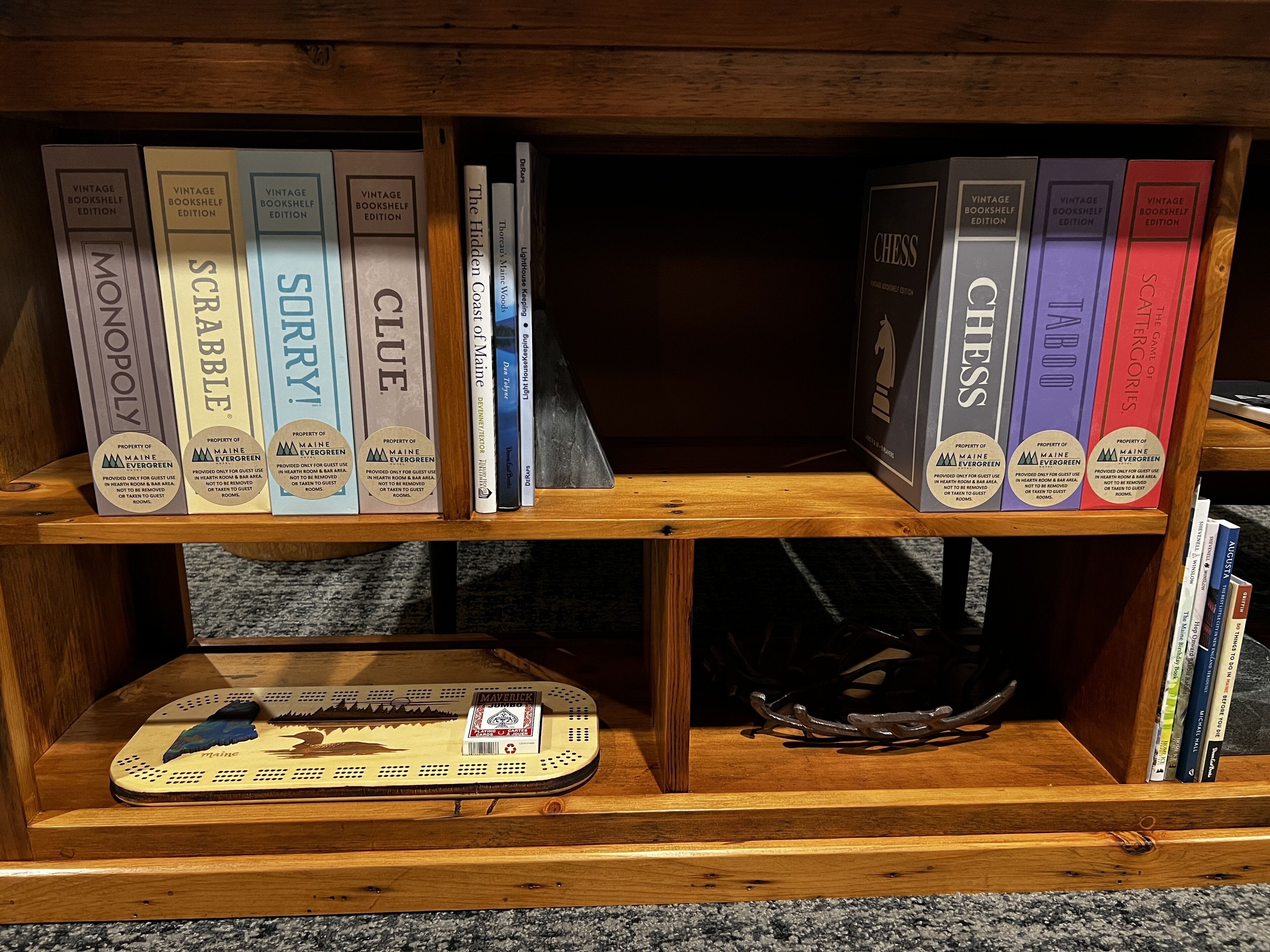 A wooden bookshelf with vintage bookshelves containing board games like Monopoly, Scrabble, Clue, and Chess.