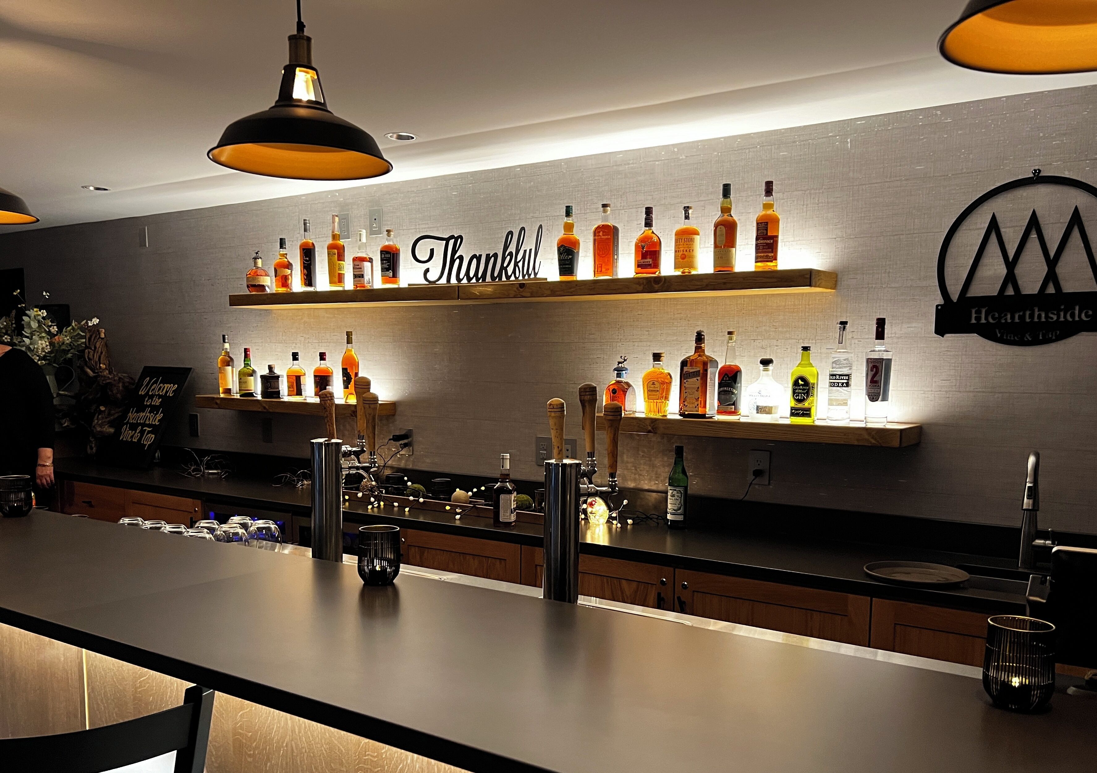 A bar area with shelves of liquor bottles, a 'Thankful' sign, and a 'Hearthside' logo.