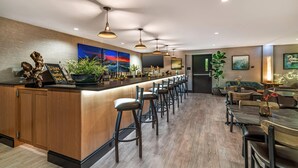A modern bar area with a long counter, multiple stools, and a seating area with tables and chairs. - Maine Evergreen Hotel, an Ascend Collection Hotel (Augusta)