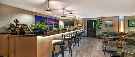 Een moderne bar met een lange toonbank, meerdere barkrukken en een zithoek met tafels en stoelen.