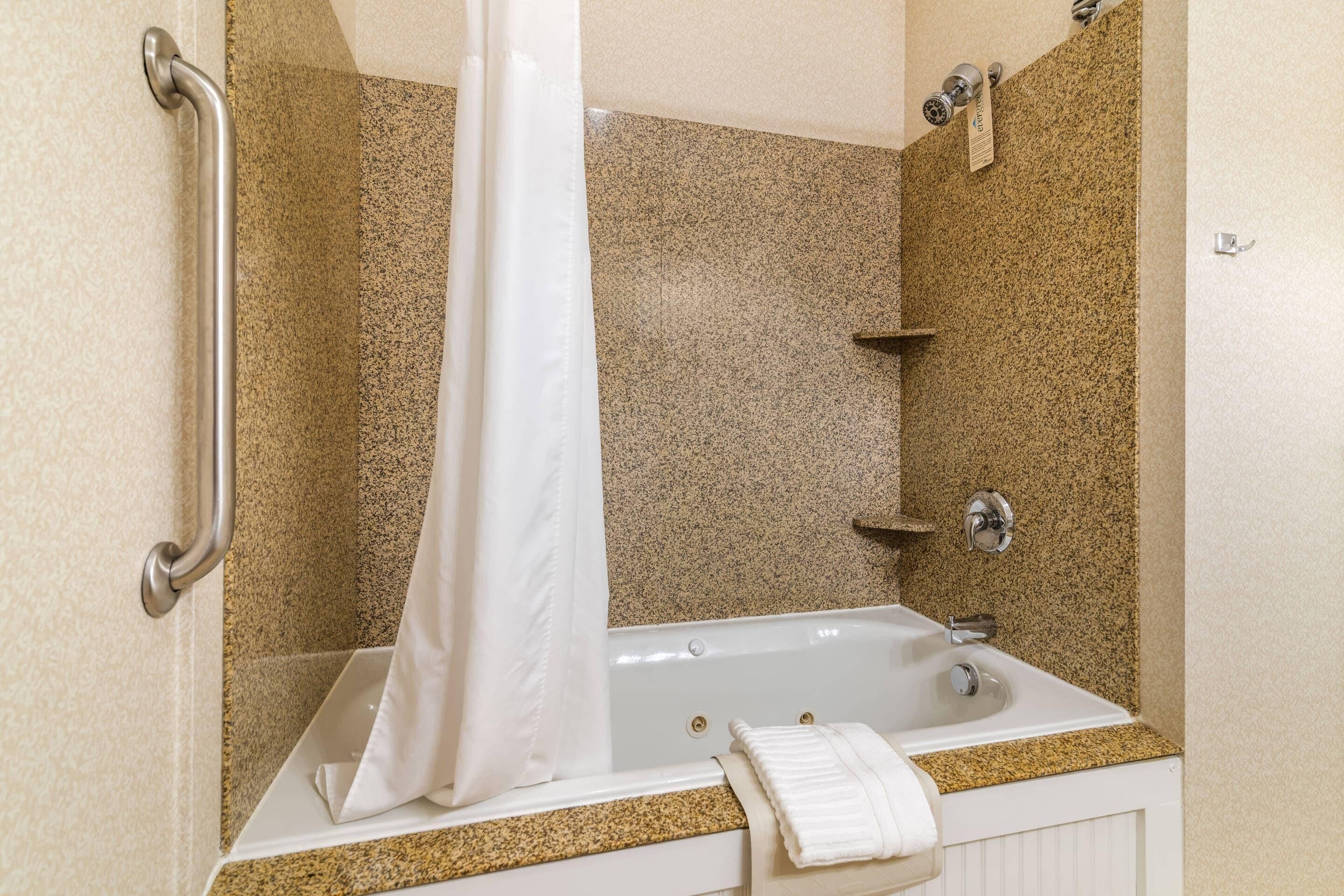 A bathroom with a bathtub, a shower curtain, a towel, and a handrail.