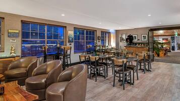 A modern hotel lobby with leather chairs, wooden tables, and large windows with blinds.