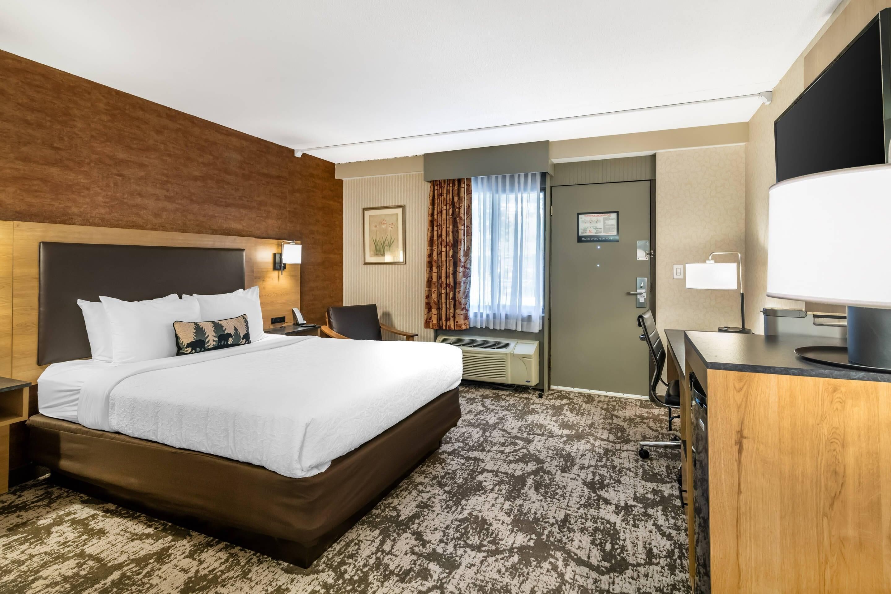 Habitación de hotel con una cama grande, un escritorio, un televisor de pantalla plana y una ventana con cortinas.