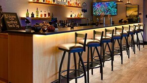 A bar area with a long counter, multiple stools, and a TV screen displaying a colorful image. - Maine Evergreen Hotel, an Ascend Collection Hotel (Augusta)