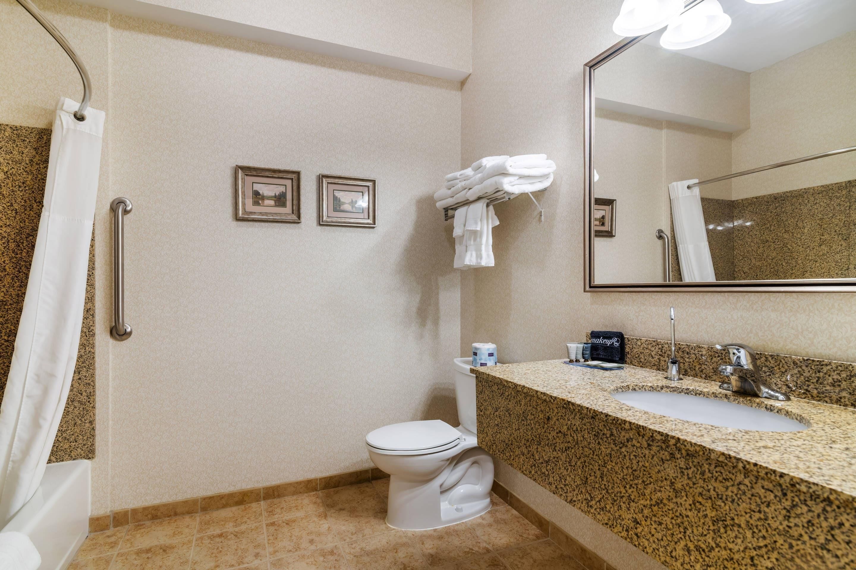 A bathroom with a toilet, sink, and shower. There are two framed pictures on the wall and a towel rack with towels.